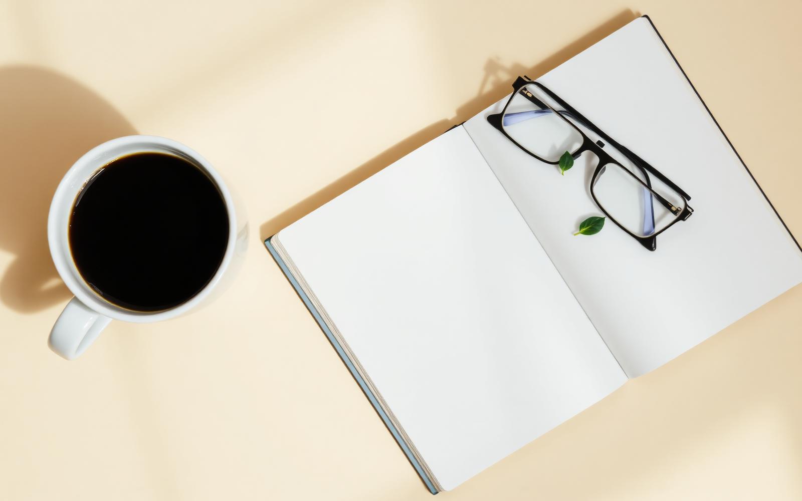 Open notebook, glasses and a cup of coffee